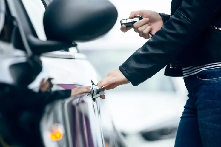 A driver pressing the unlock button on a car key fob next to a parked vehicle