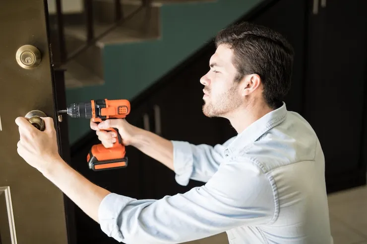 A locksmith technician using a drill to install a new deadbolt lock on a home's front door